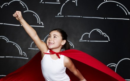 A girl in a cape with arm out and hand clenched looking like she is preparing to fly.