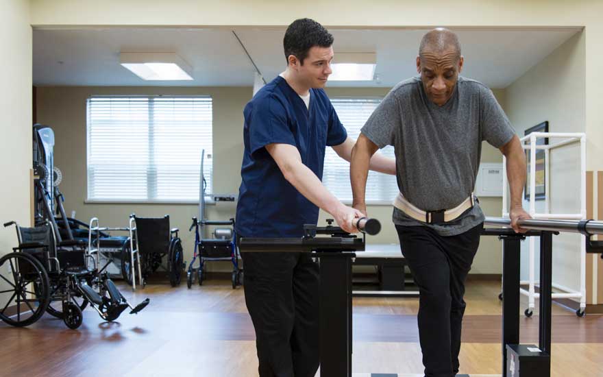 A physical therapist working with a man using parallel bars to help him walk.