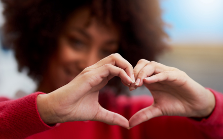 A Black female olds her hands in the shape of a heart.