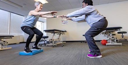 A physical therapist educating a patient on  how to perform a strength and balance exercise.