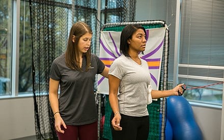 A physical therapist guides a woman through shoulder rehabilitation exercises.