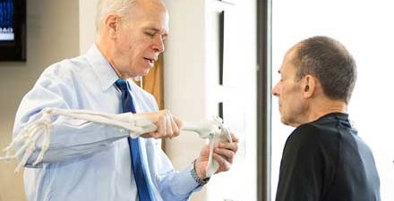 A physical therapist shows a patient an example of the bones of the elbow.