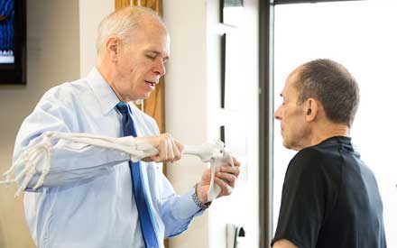 A physical therapist shows a patient an example of the bones of the elbow.