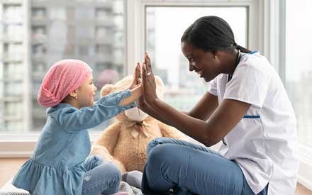 An oncologic physical therapist gives a high five to a young cancer patient.