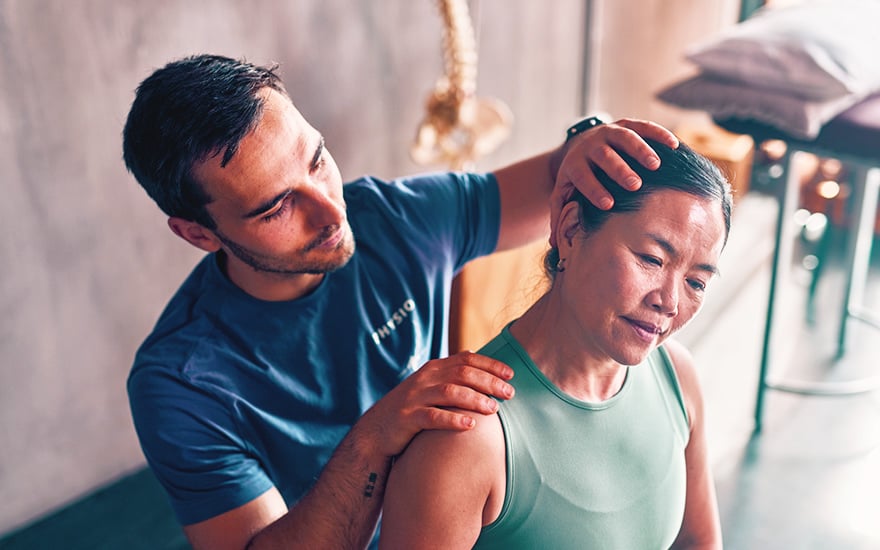 A physical therapist conducts a hands-on assessment on a woman's neck.