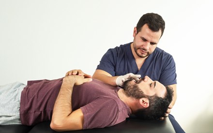 A physical therapist provides manual therapy to a man's jaw.