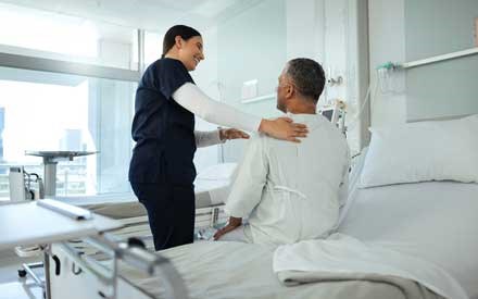 A physical therapist helping a man get out of his hospital bed.