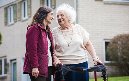 Virginia, using a walker outdoors, smiling toward another woman.