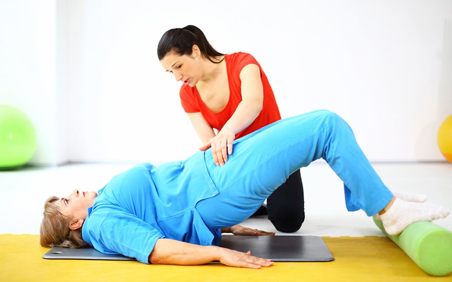 A physical therapist guides a female patient through leg and core strengthening exercises