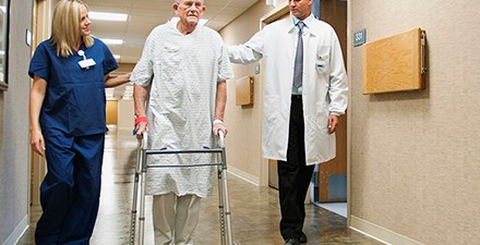 A patient walking the halls of a hospital with his physical therapist and doctor.