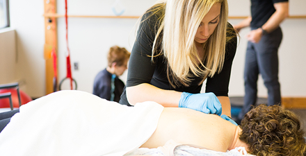 A PT performing dry needling on a person's shoulder.