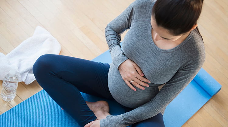 Top view of a pregnant woman in sportswear sitting on a yoga mat